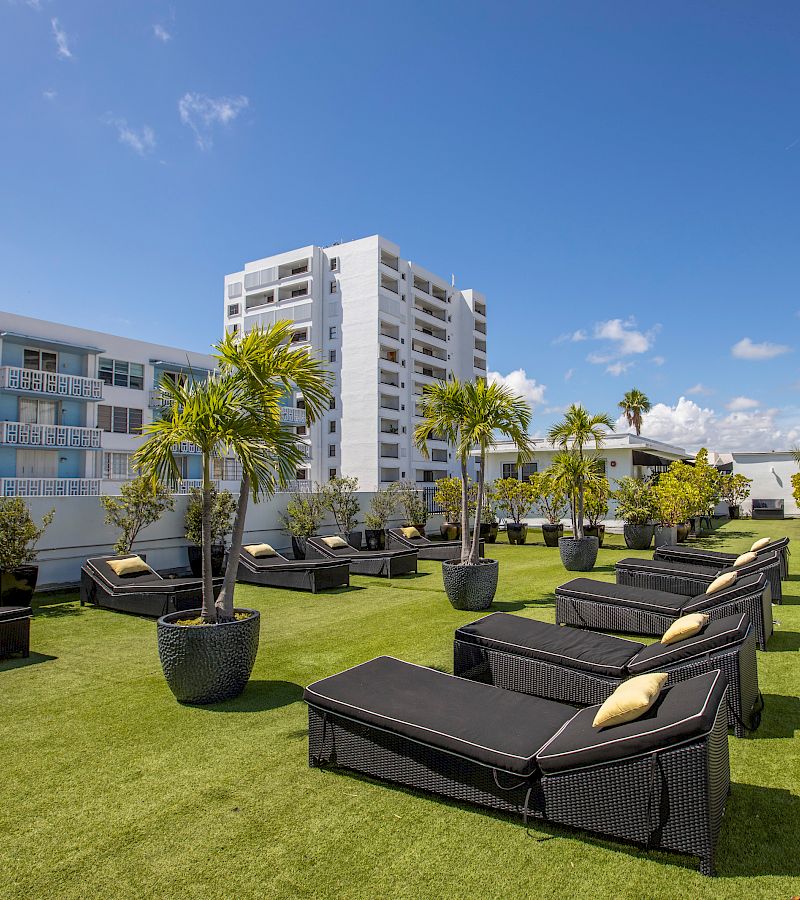 A resort-style pool area with artificial turf, lounge chairs, and potted palm trees.