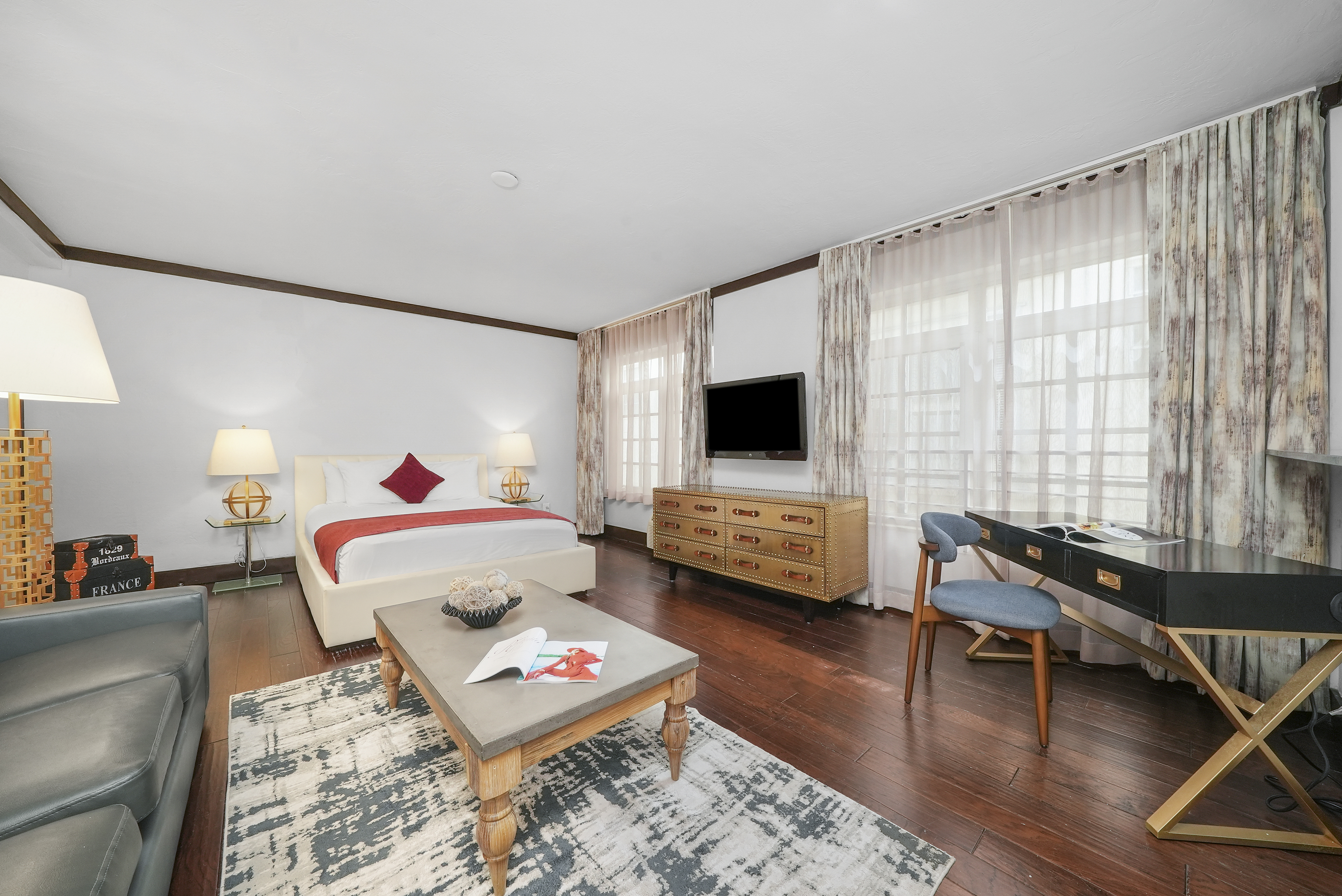A wide view of a hotel suite with a king-sized bed, a sofa, a desk, and a TV.