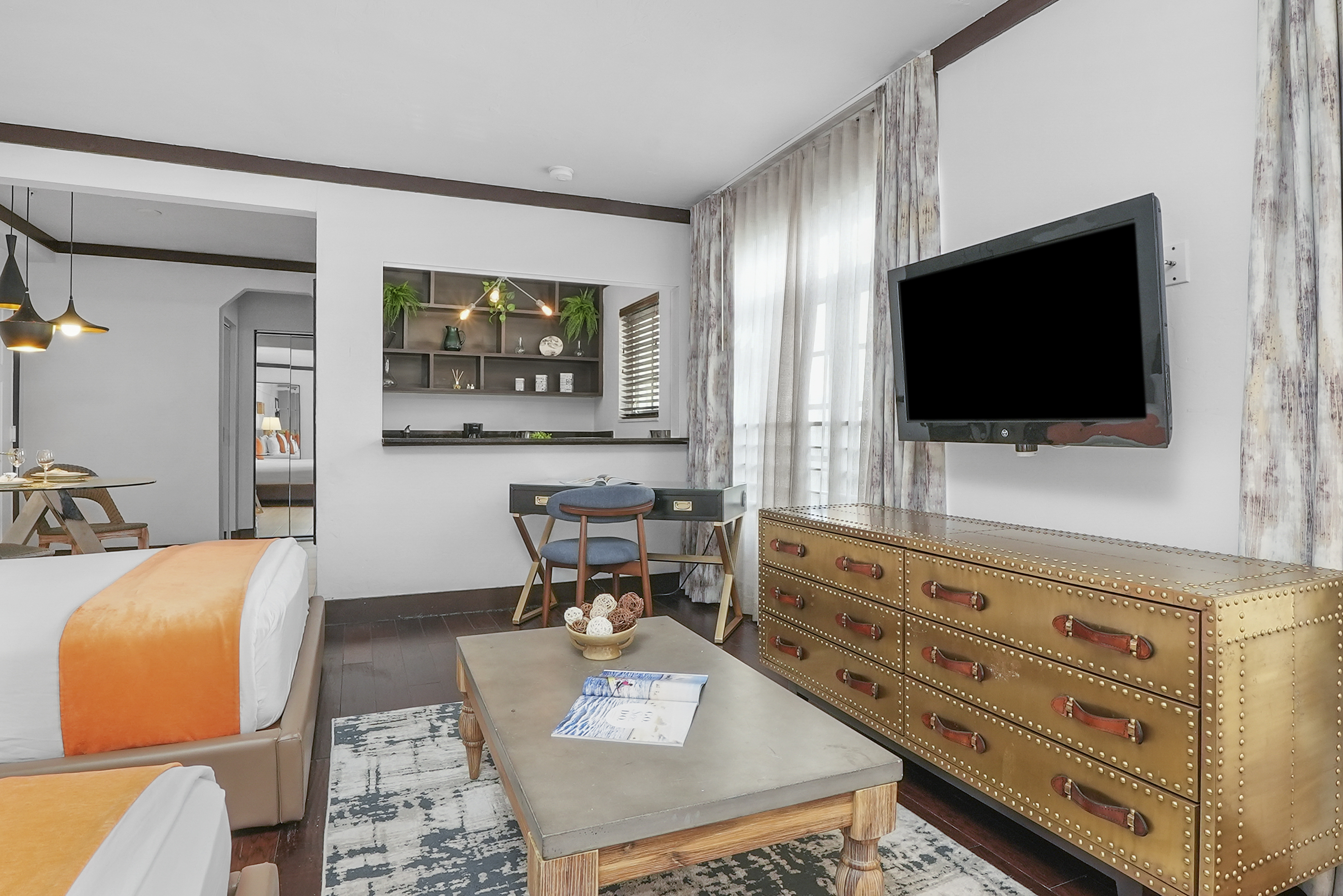 A wide view of a hotel room with a bed, TV, dresser, and coffee table.