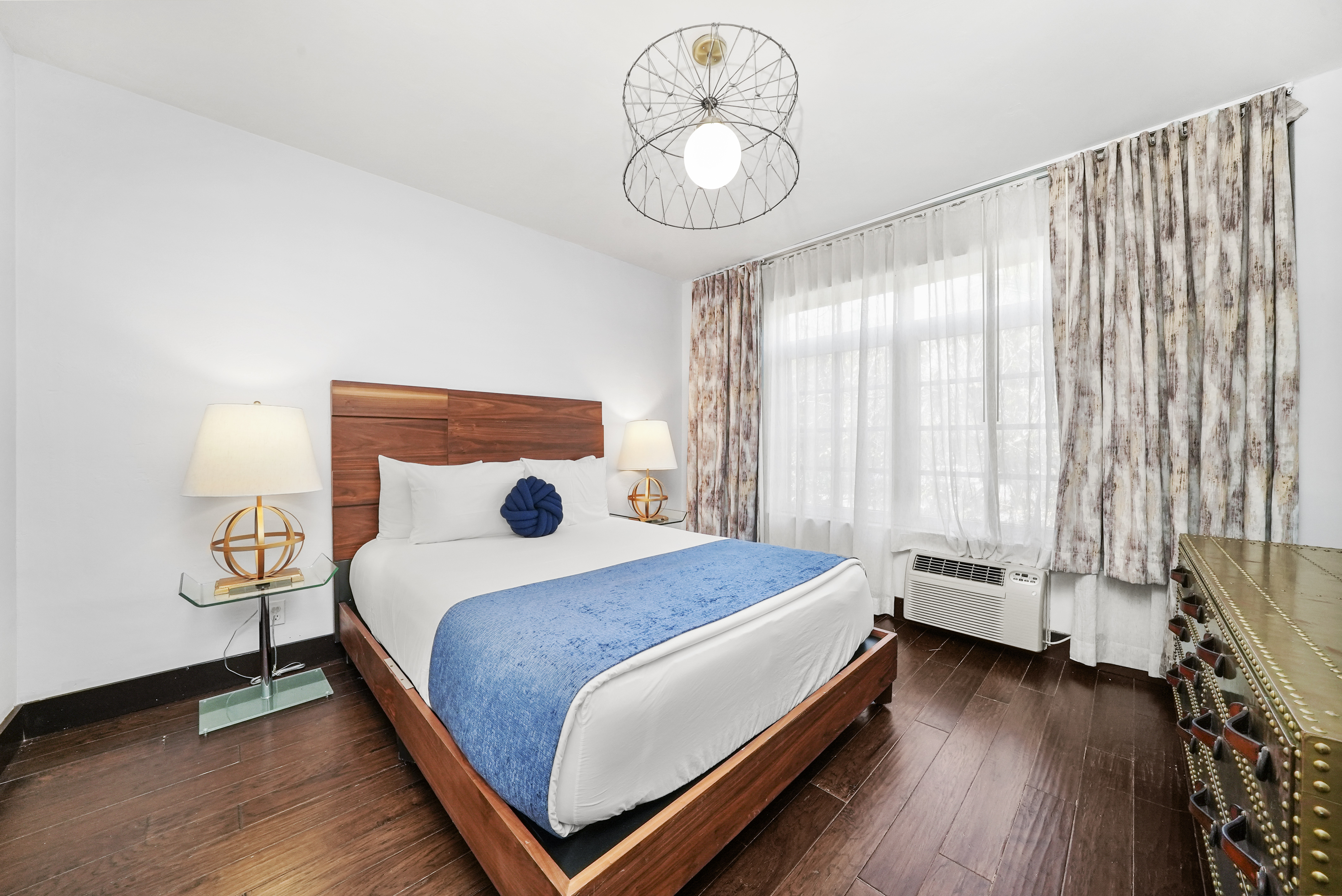 A hotel room with a bed, two lamps, a window with curtains, and a dresser.