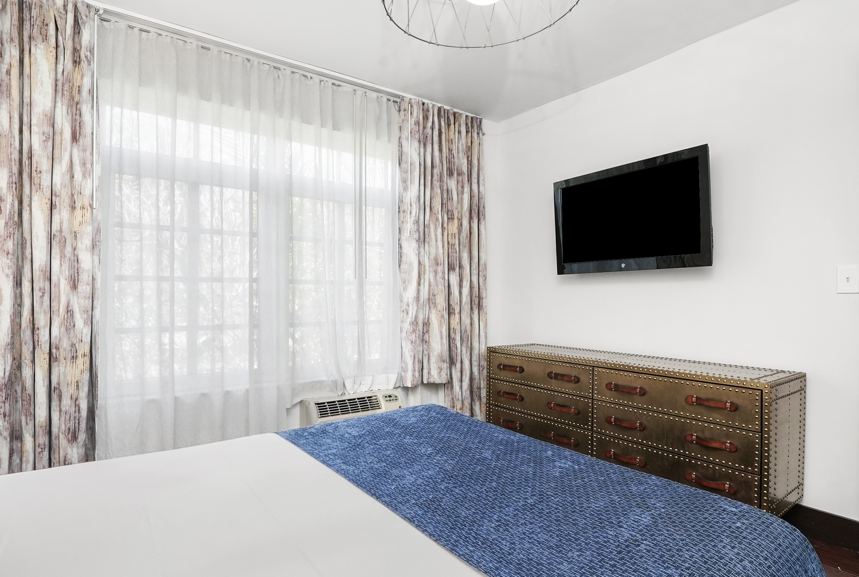 A hotel room with a bed, dresser, TV, and window
