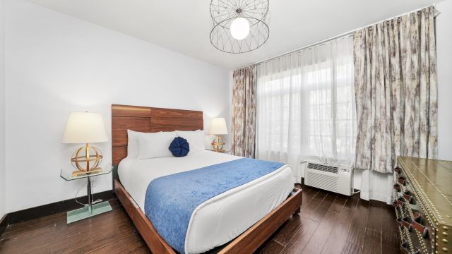 A hotel room with a king-size bed, a dresser, and a window