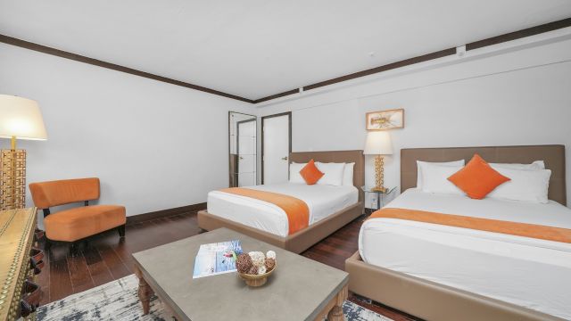 A hotel room with two twin beds, a coffee table, an armchair, and lamps.