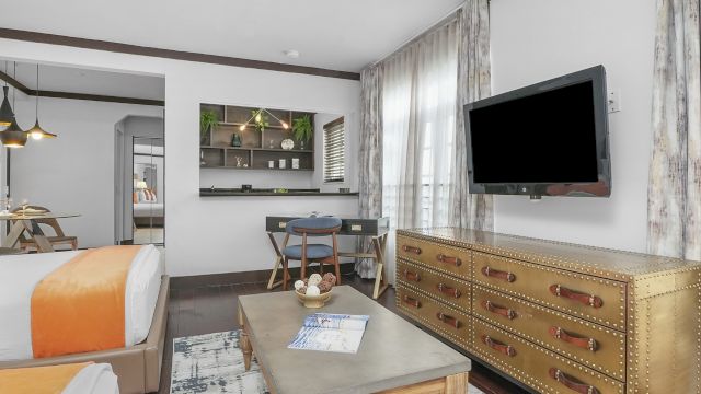 A wide view of a hotel suite with a bed, desk, TV, and coffee table.