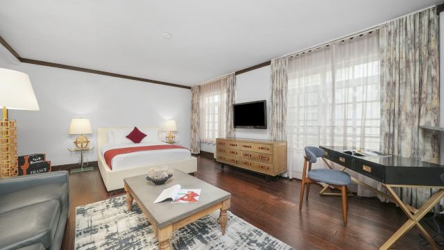 A wide view of a hotel suite with a bed, desk, sofa, and coffee table.