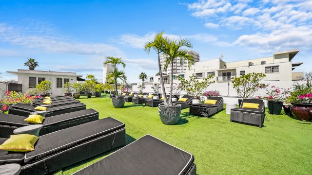 A rooftop lounge with black lounge chairs and yellow pillows on artificial turf.