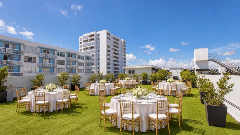 A grassy rooftop with round tables set for an event, surrounded by buildings and a blue sky.